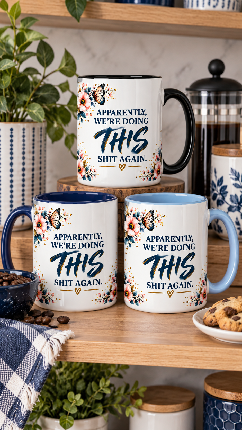 Three ceramic mugs with the humorous phrase 'APPARENTLY, WE'RE DOING THIS SHIT AGAIN.' printed on them, displayed on a wooden shelf with coffee-themed props including a coffee pot, beans, and cookies.