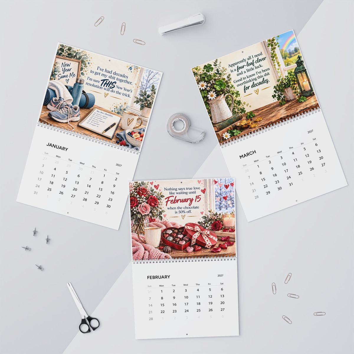 Three printed monthly calendar pages with inspirational quotes and floral desk scenes, arranged on a light gray surface with paper clips, tape, scissors, and a pen around them.