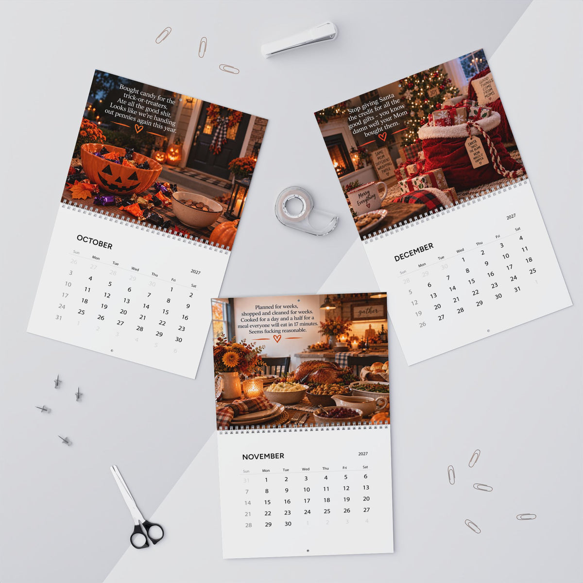 Three spiral-bound monthly calendar pages with holiday-themed printed photos and month grids are arranged on a light gray surface with paper clips, a tape measure, scissors, and a pen around them.